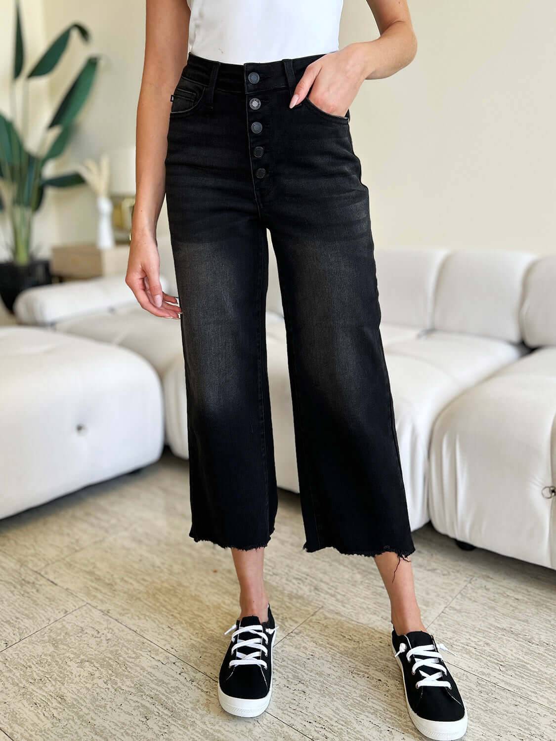 a woman standing in a living room wearing a white shirt and black jeans