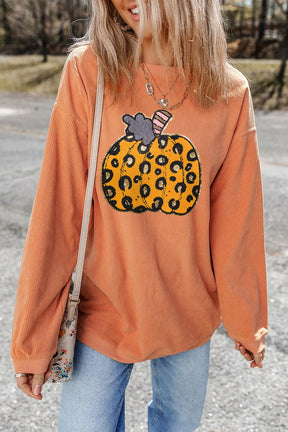 a woman wearing an orange sweater with a leopard print pumpkin on it