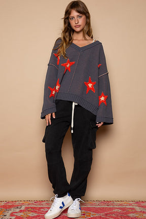 a woman standing in front of a wall wearing a sweater with red stars on it