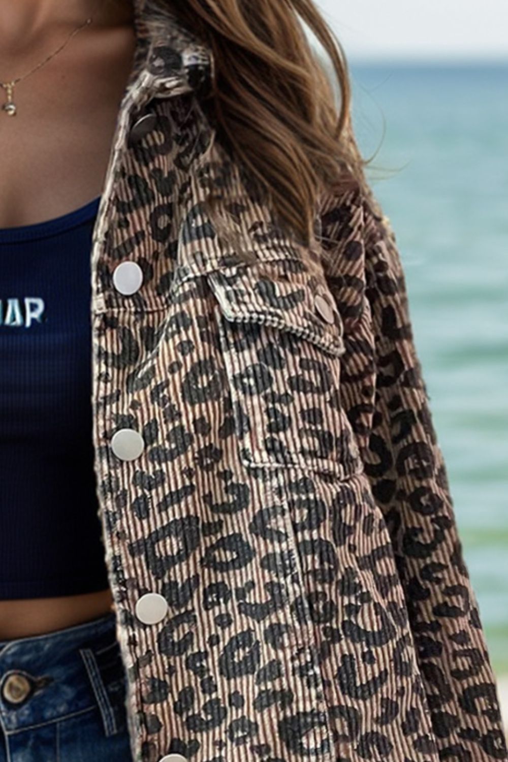 a woman standing on a beach wearing a leopard print jacket