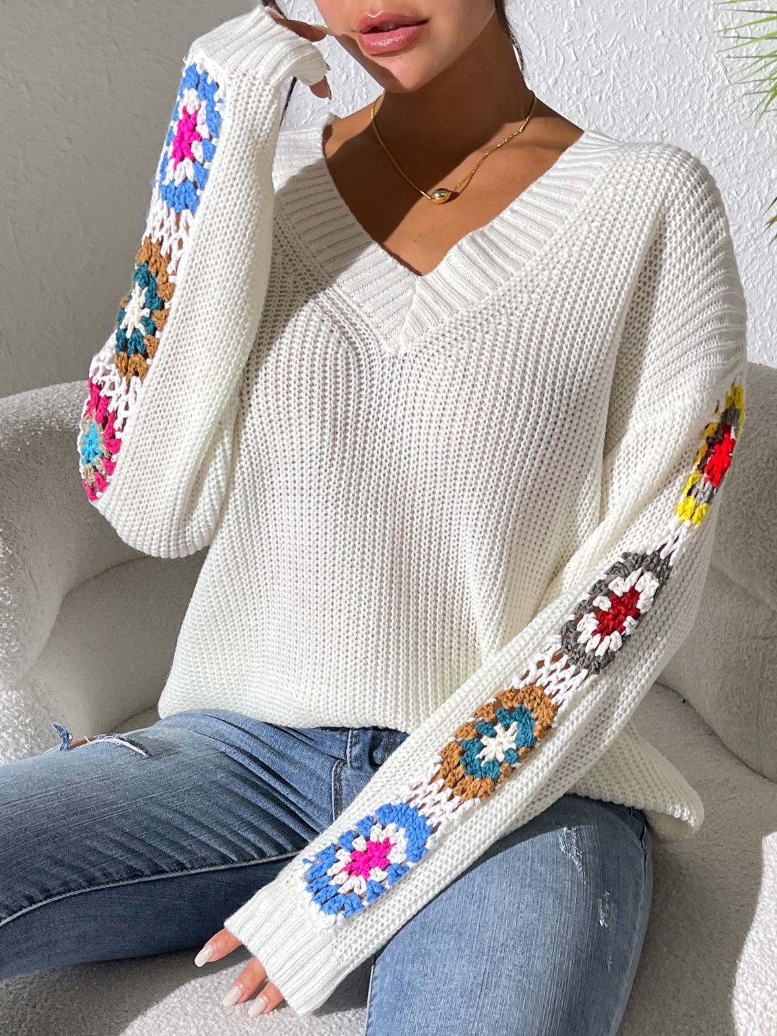 White V-neck sweater featuring crochet flower designs on sleeves.